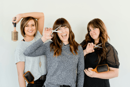 Three salon stylists posing with brushes and scissors